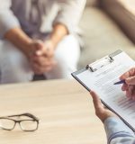 Cropped image of depressed man at the psychotherapist. Doctor is making notes while listening to his patient